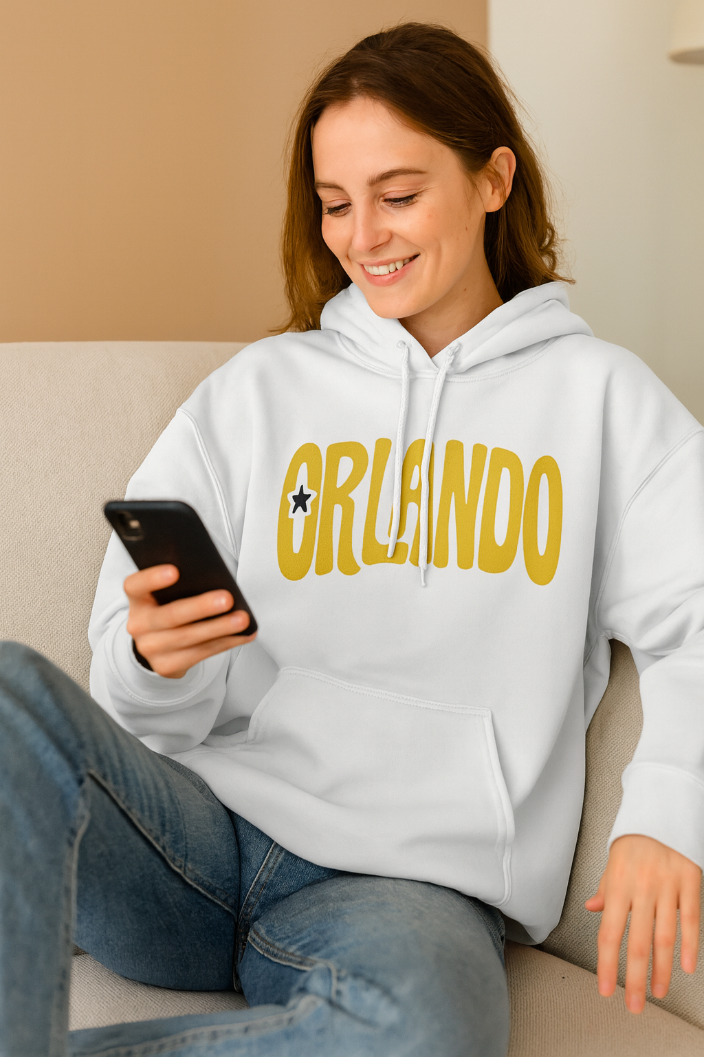 Woman wearing a white hoodie with 'Orlando' printed on it, sitting on a couch and looking at her phone.
