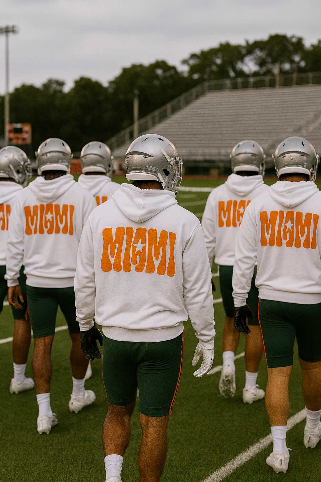 Group of football players wearing white hoodies with 'MIAMI' printed on the back, standing on a football field.