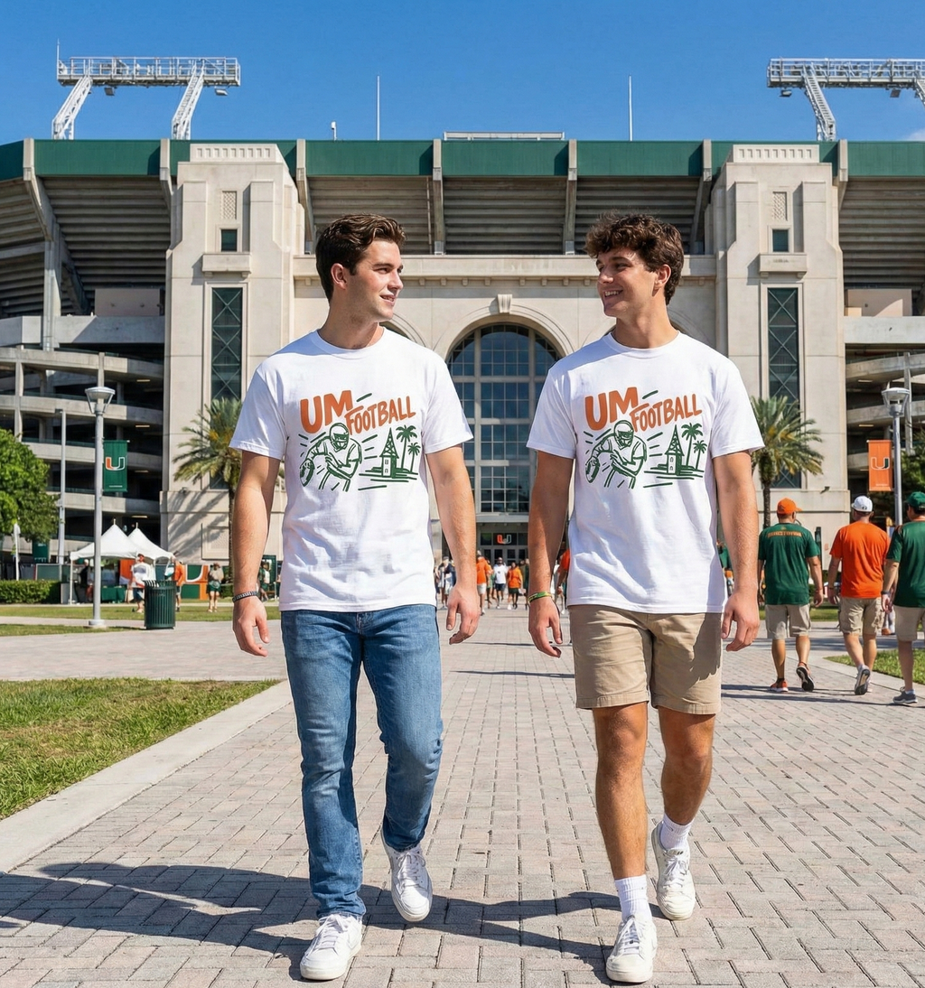 Two individuals walking on a path in front of a stadium wearing UM Football t-shirts.