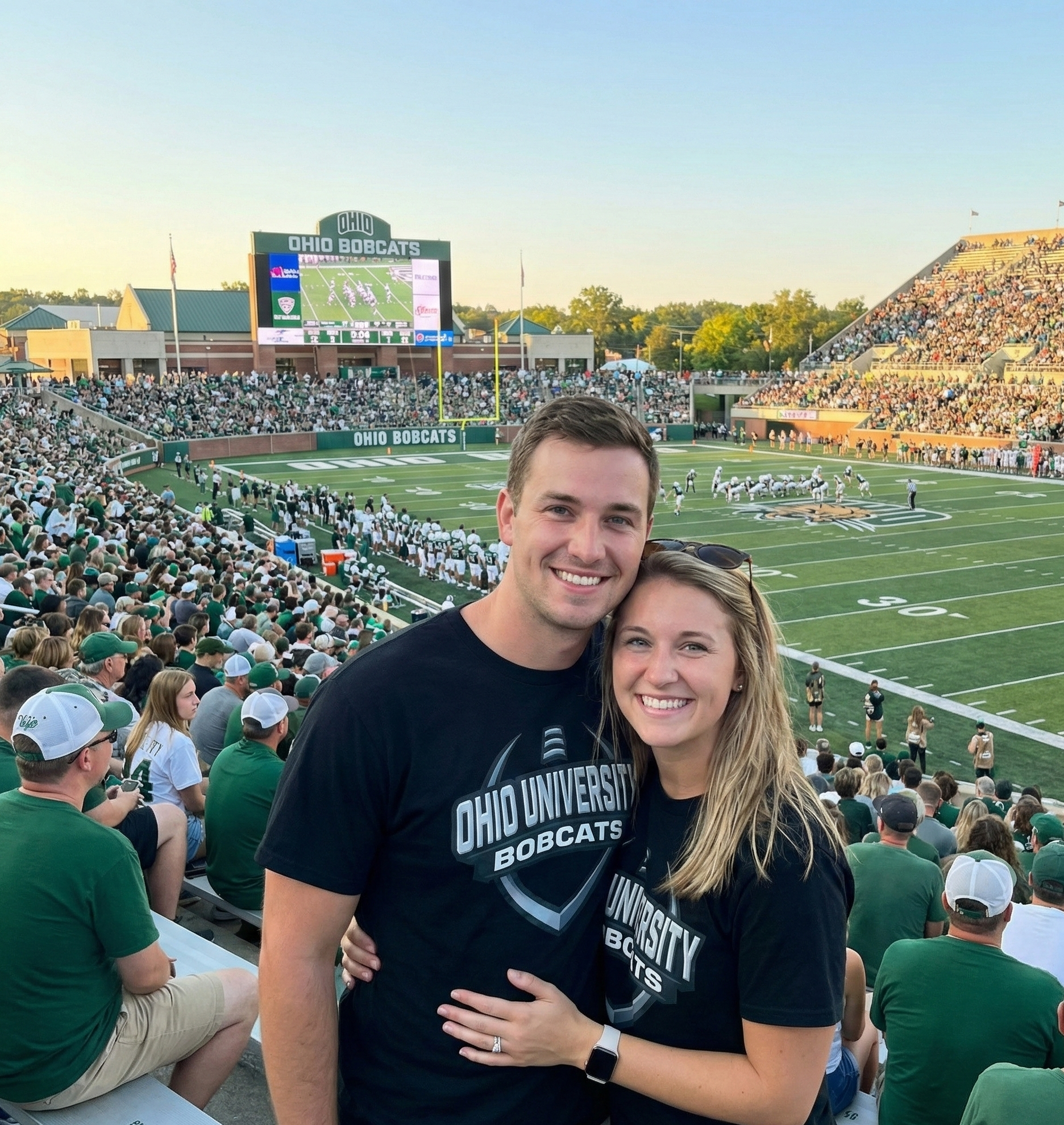 Two people posing for a photo at a football stadium with 'Ohio Bobcats' branding.