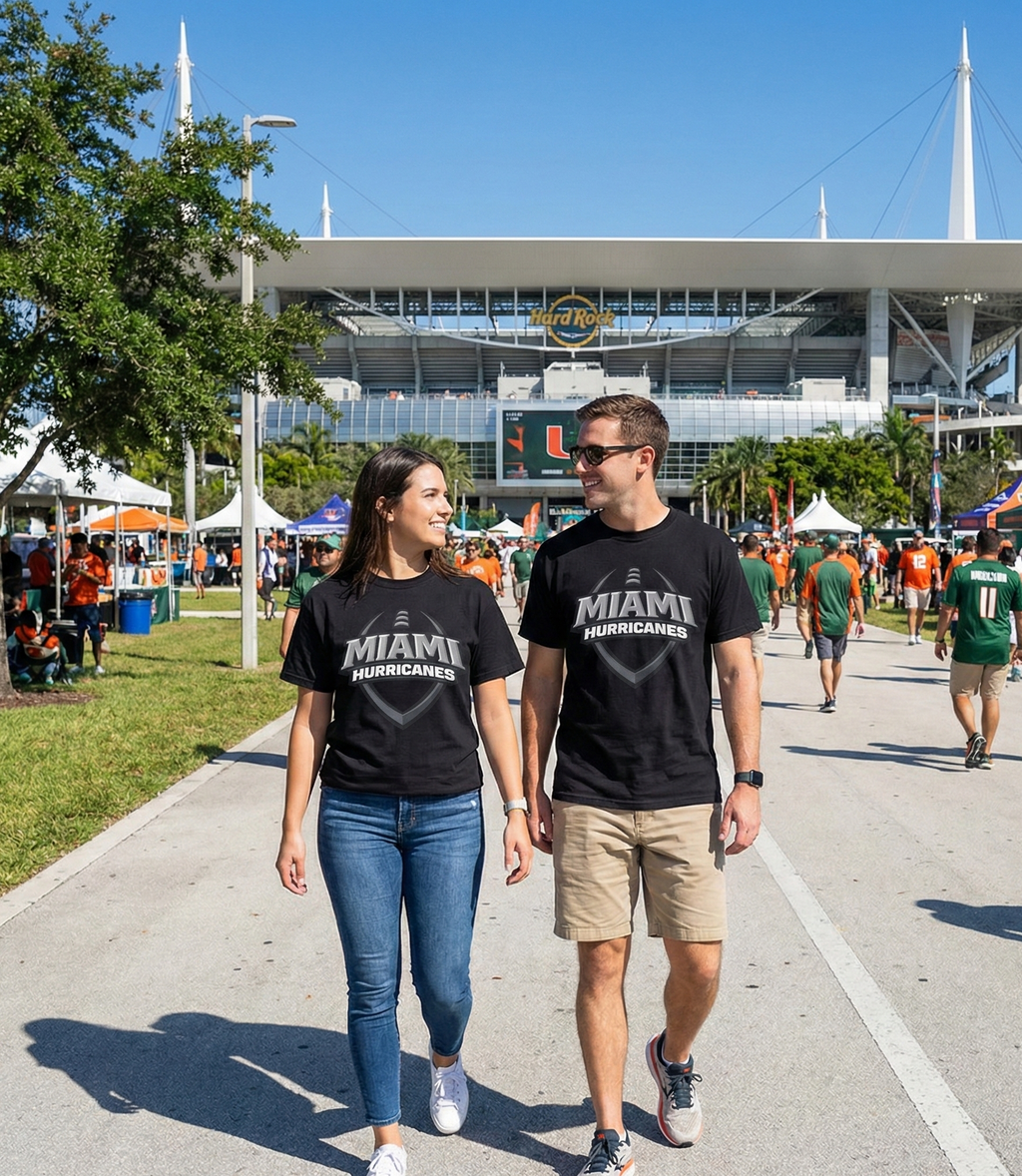 Two people wearing 'Miami Hurricanes' shirts walking on a path with a stadium in the background.